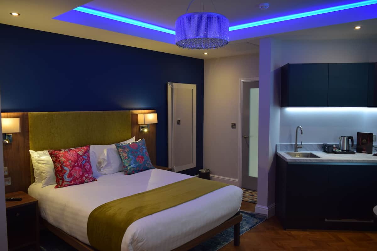 Habitación de hotel moderna con una cama grande, una mesita de noche, un escritorio integrado con lavamanos y un espejo sobre el escritorio.
