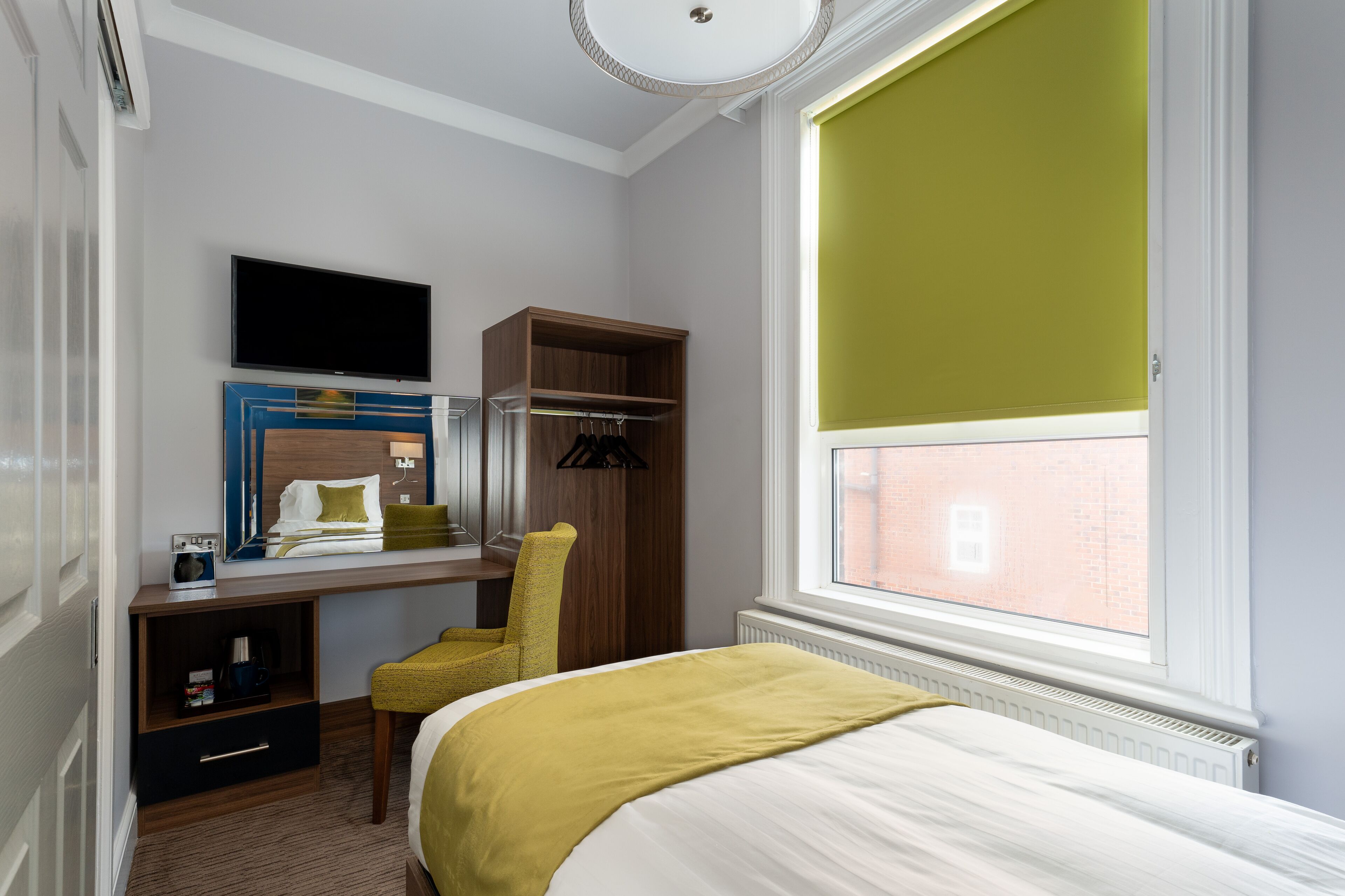 Habitación de hotel con cama, escritorio con silla, televisión y ventana con vista a un edificio de ladrillo.