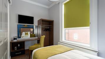 Habitación de hotel con cama, escritorio con silla, televisión y ventana con vista a un edificio de ladrillo.