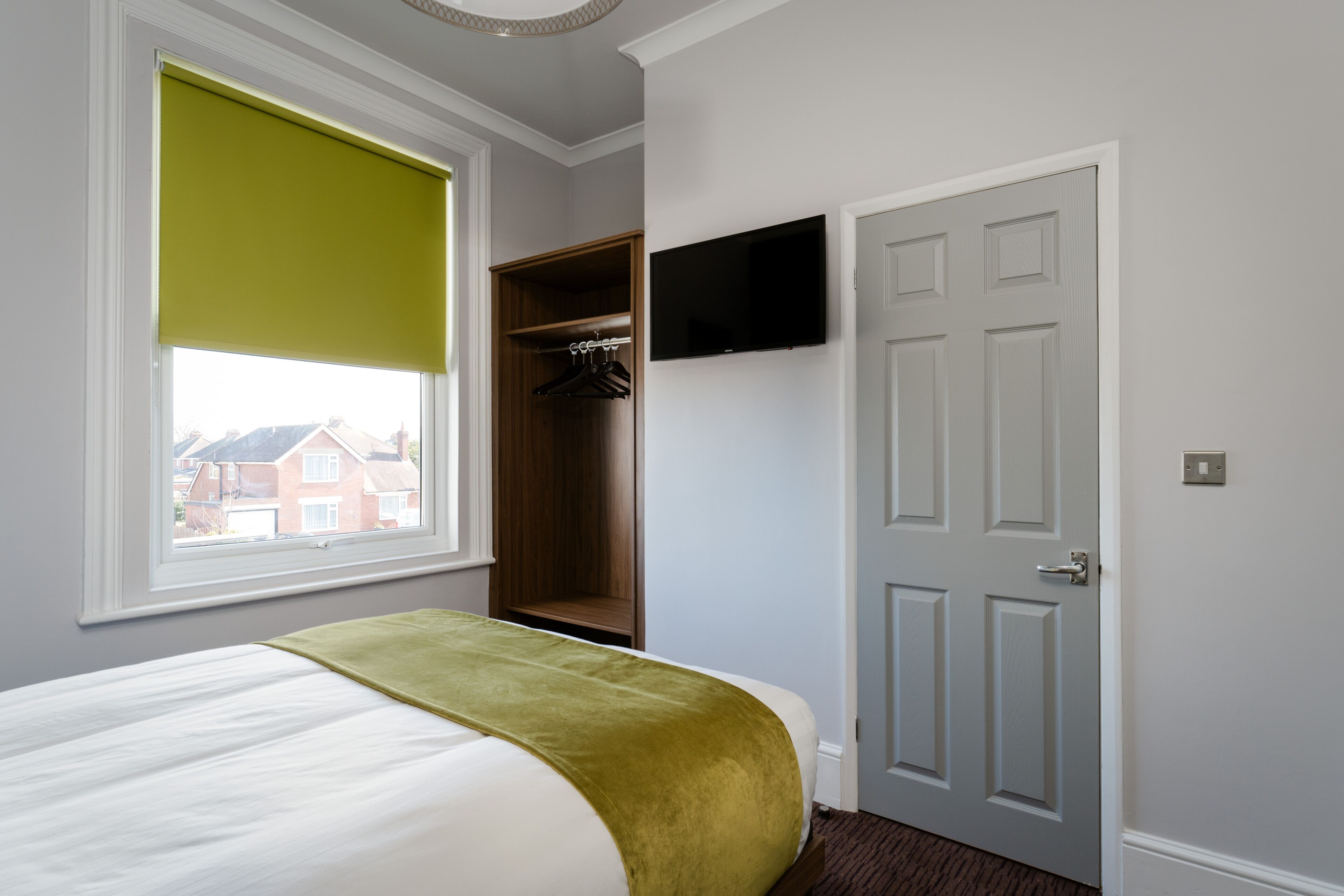 Ein Schlafzimmer mit Bett, Kleiderschrank, Wandfernseher und einem Fenster mit Jalousie.