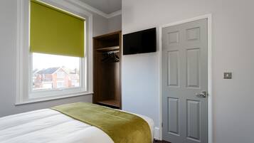 Un dormitorio con cama, armario, televisor montado en la pared y ventana con persiana.