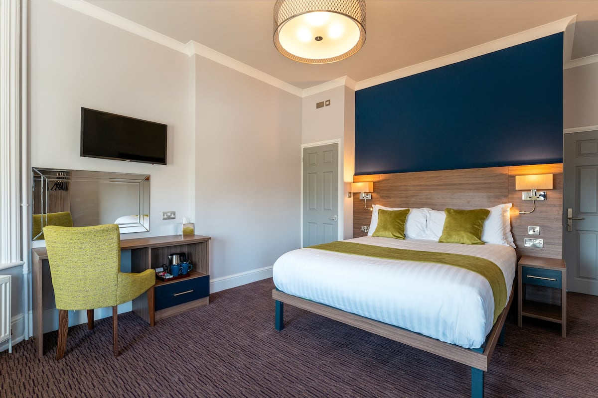 Una habitación de hotel con una cama, un escritorio con una silla, un televisor y una lámpara.