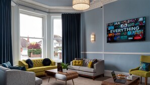 Una sala de estar moderna con un televisor grande mostrando la interfaz de un servicio de streaming, un sofá, una mesa de centro y una zona de estar cómoda.