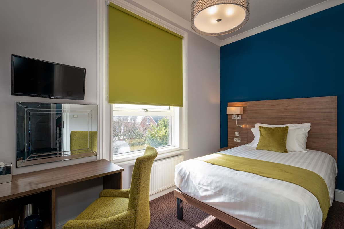 Una habitación de hotel con una cama, un escritorio, una silla, un televisor y una ventana con vistas al exterior.