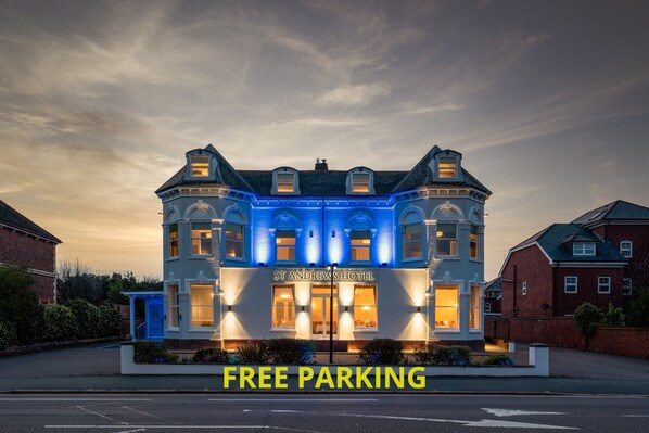 Un hotel con un letrero llamativo que dice "ESTACIONAMIENTO GRATIS" y un estilo arquitectónico clásico.