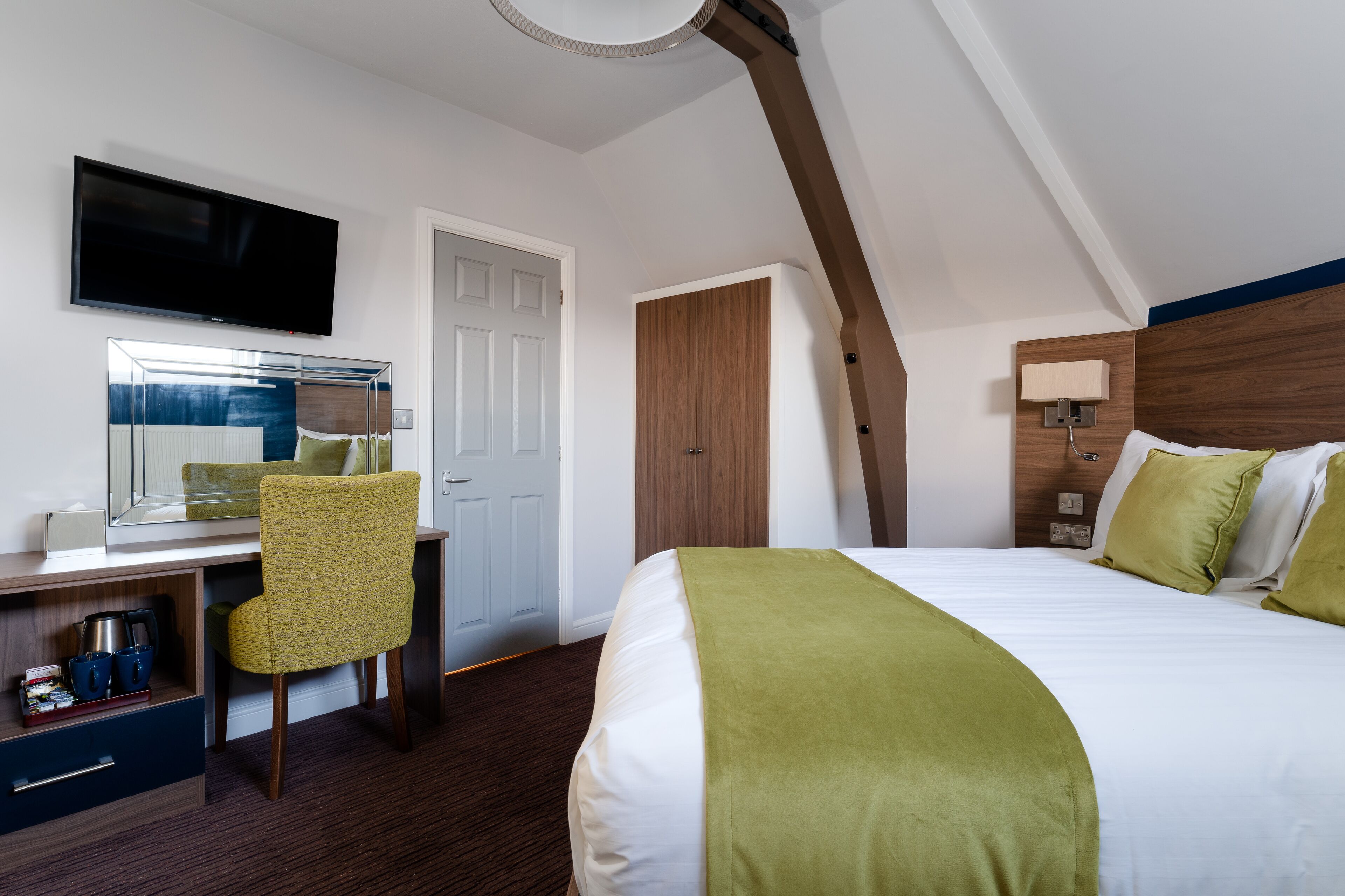 A hotel room with a bed, a desk with a chair, a television, and a wooden headboard.