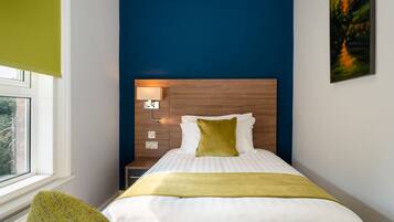 A neatly arranged hotel room with a bed, bedside lamp, and a window.