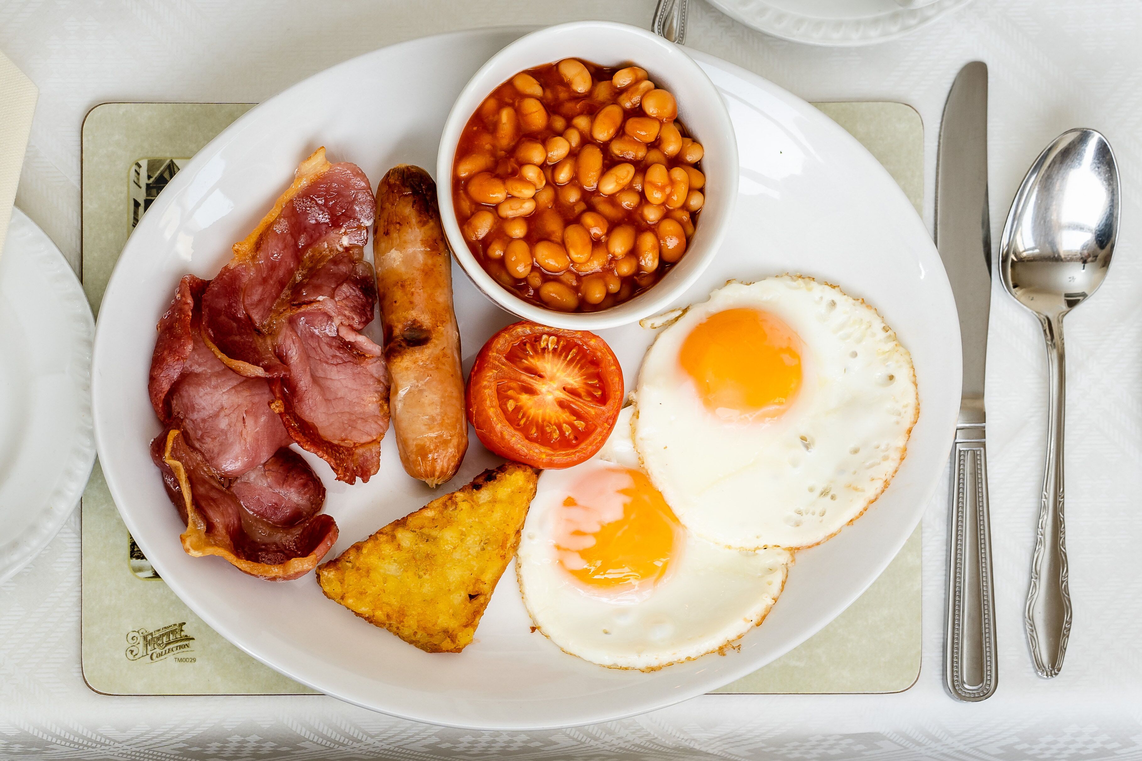 A plate with bacon, sausages, eggs, beans, and a tomato.