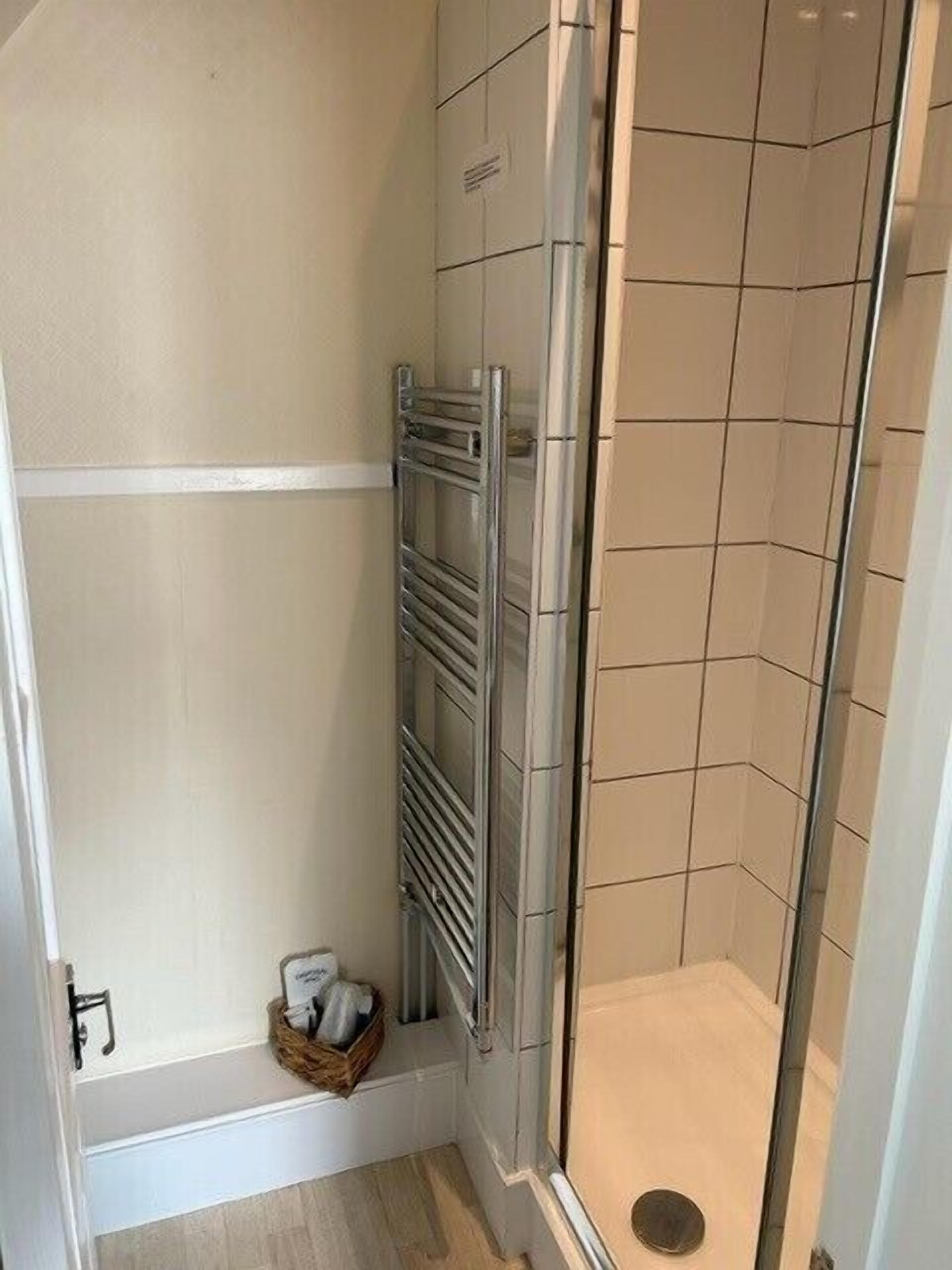 A corner shower with a glass door, a metal towel rack, and a small basket with toiletries.