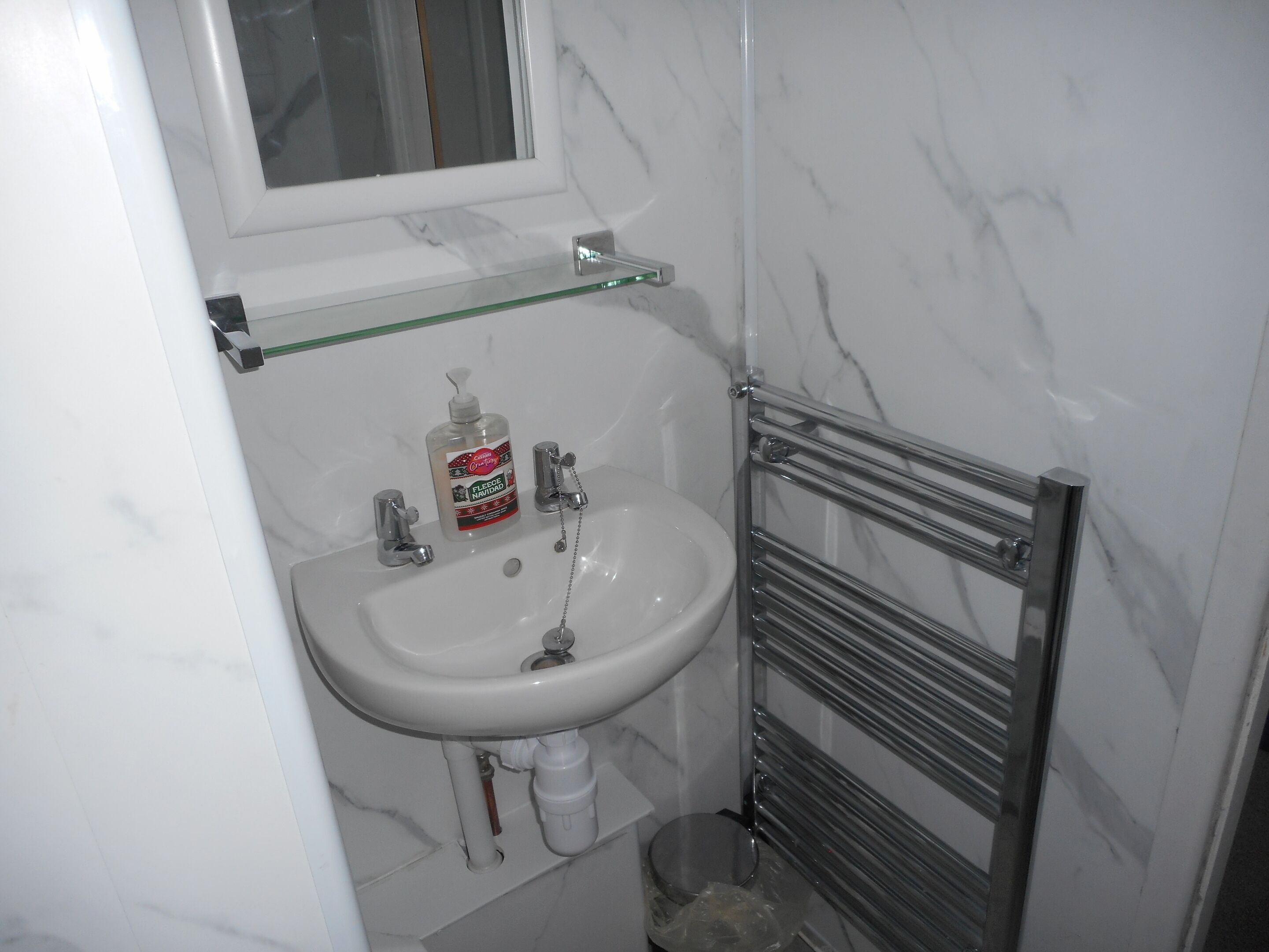 A bathroom with a white sink, a glass shelf above it, a bottle of liquid soap, and a chrome towel rack.