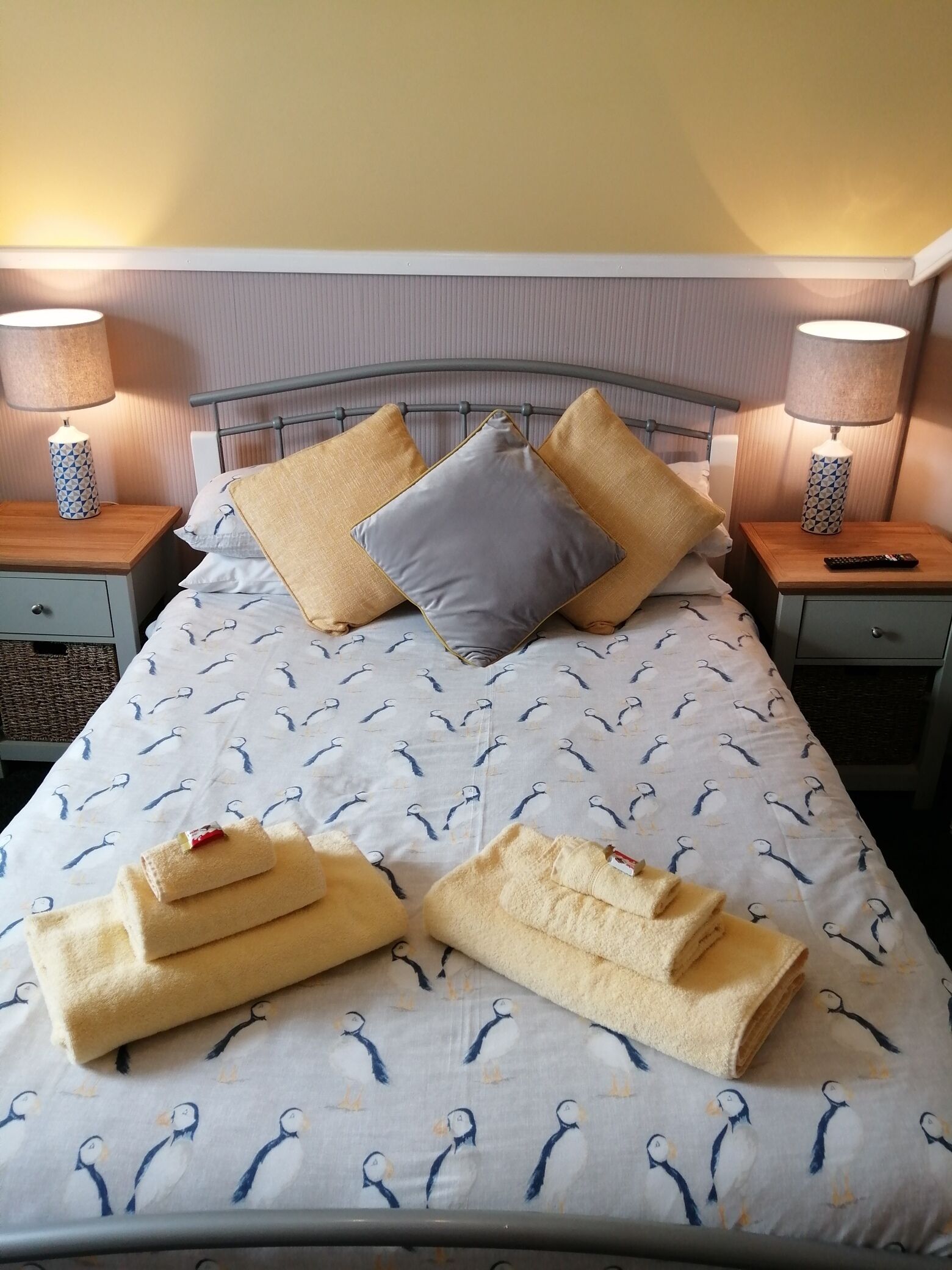 A neatly made bed with a patterned duvet, pillows, and folded towels.