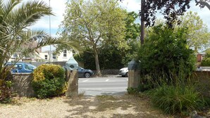 A gravel driveway leading to a residential area with parked cars and a stone wall. - The George B&B (Weymouth)