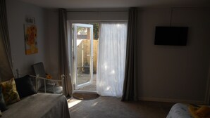 A hotel room with a bed, a chair, a television, and a sliding glass door leading to an outdoor area. - The George B&B (Weymouth)