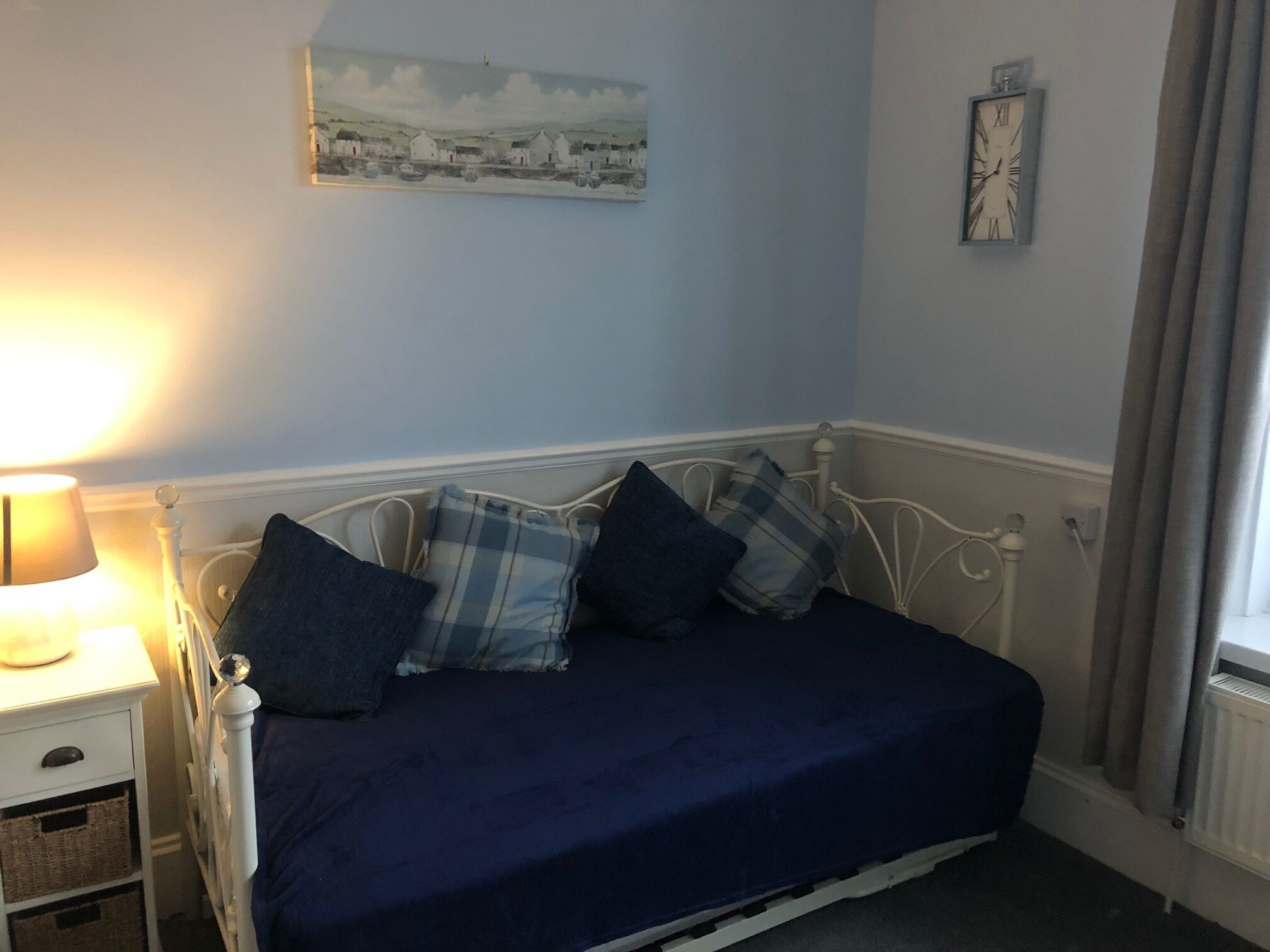 A bedroom with a bed, a bedside lamp, a painting, and a clock on the wall.