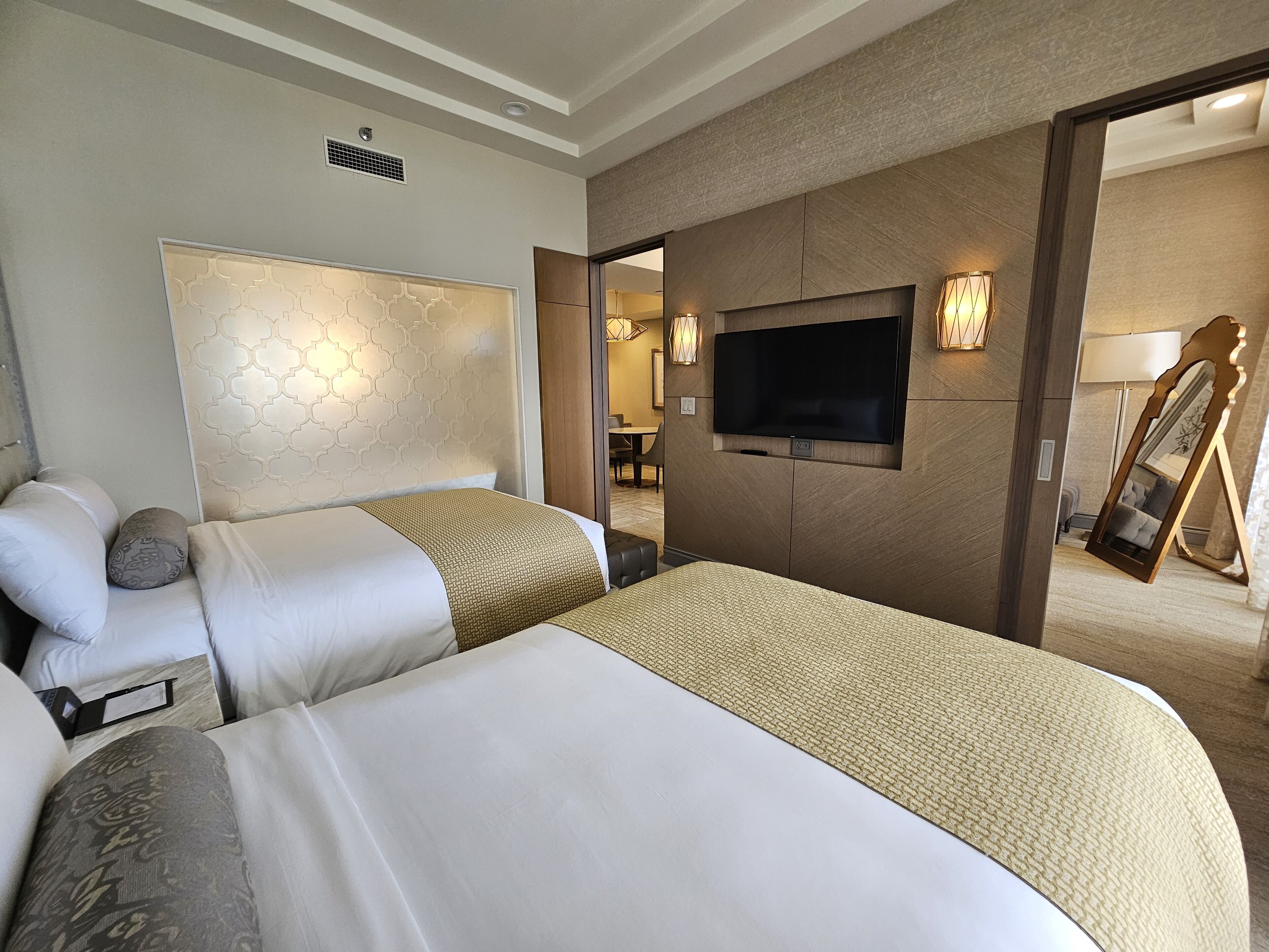 A hotel room with two beds, a TV, a mirror, and a view into the bathroom.