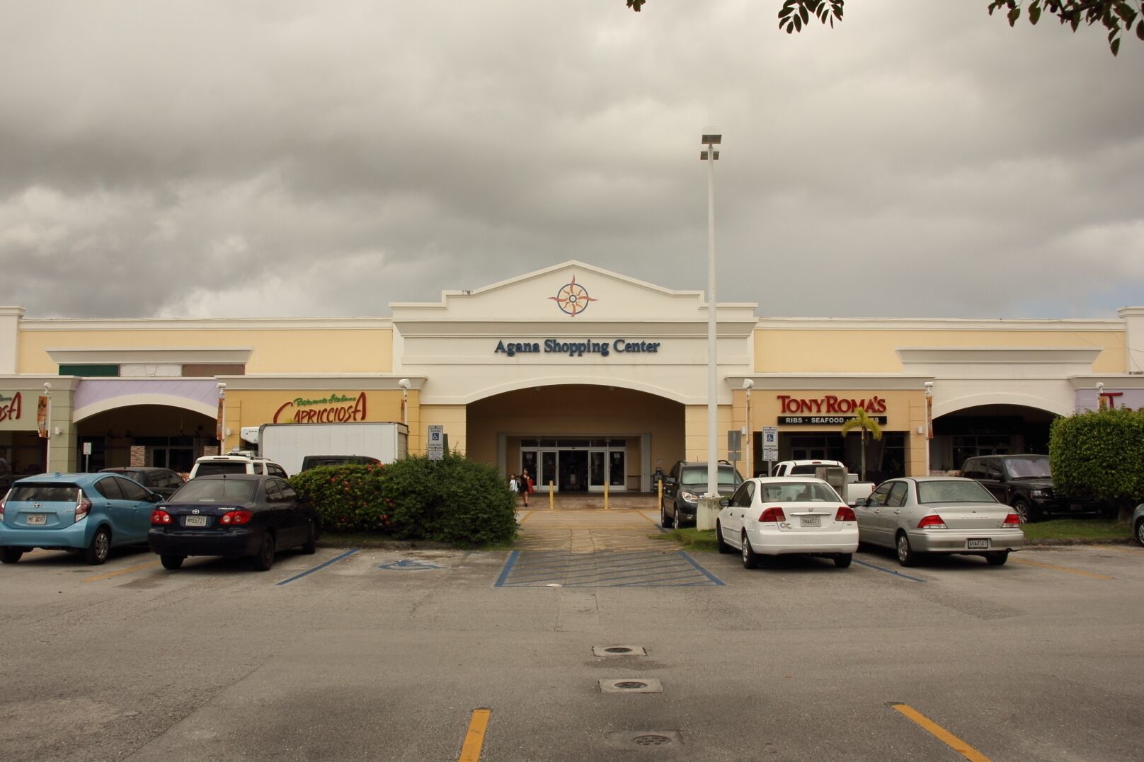 El centro comercial Agana con varias tiendas, incluyendo Tony Roma's, y un estacionamiento con varios autos.
