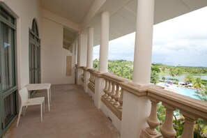 A balcony with white chairs, a view of a pool and palm trees, and a clear sky.