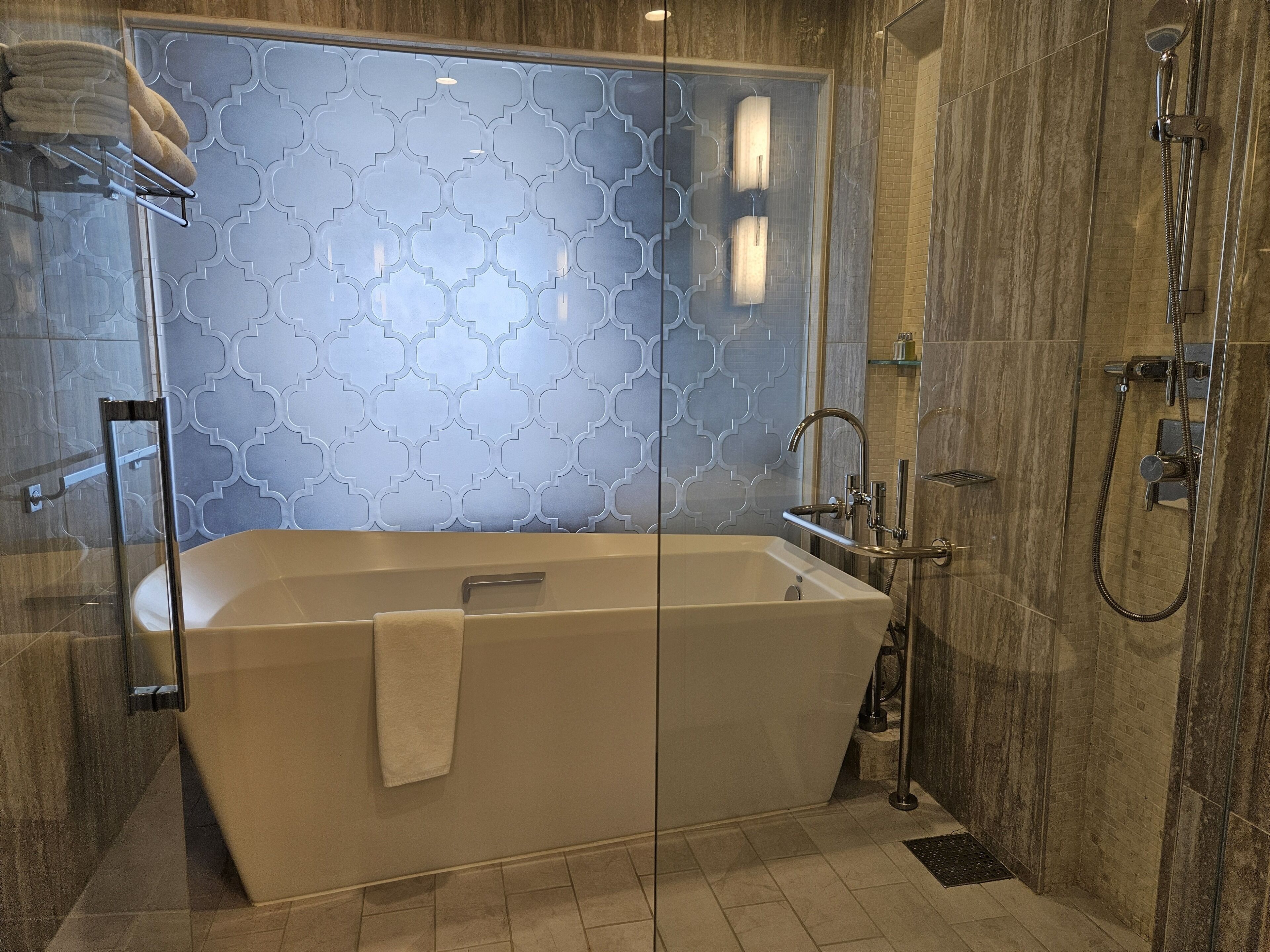 A modern bathroom with a freestanding bathtub, a glass shower enclosure, and a patterned wall.