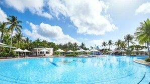 A large, clear swimming pool with lounge chairs and umbrellas, surrounded by palm trees and a clear sky. - Leopalace Resort Guam (Yona)