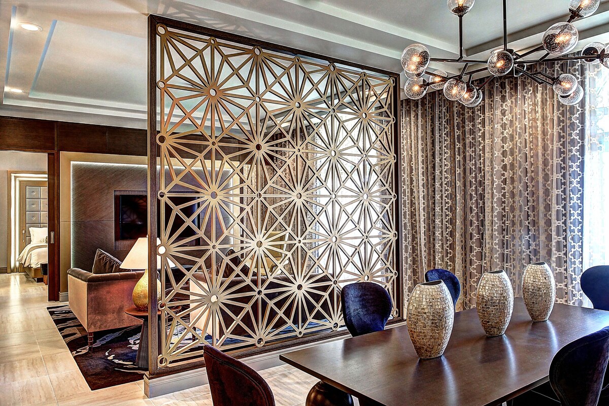 A modern hotel room with a geometric patterned partition, a dining table with vases, and a chandelier.