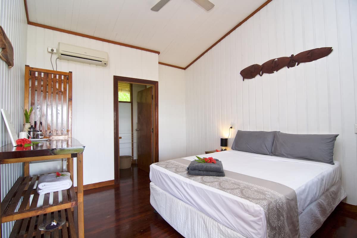 Habitación de hotel con una cama grande, un escritorio de madera, una silla y una mesita con un jarrón y flores.