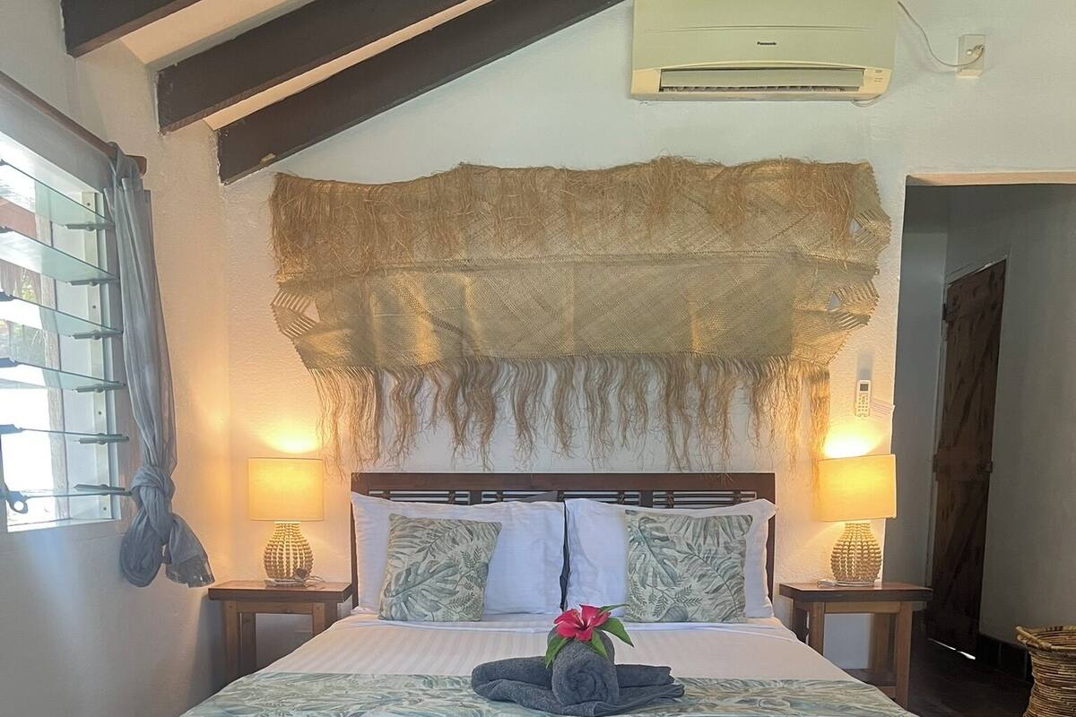 Una cama grande con estructura de madera, dos lámparas de noche, un cabecero decorativo y un aire acondicionado de pared.