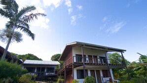 A two-story house with a balcony, surrounded by lush greenery and a palm tree. - Deco Stop Lodge (Luganville)