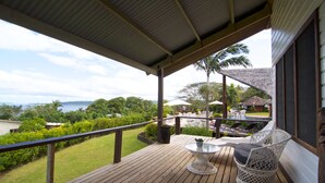 A wooden deck with a glass table and white wicker chairs, overlooking a pool and lush greenery. - Deco Stop Lodge (Luganville)