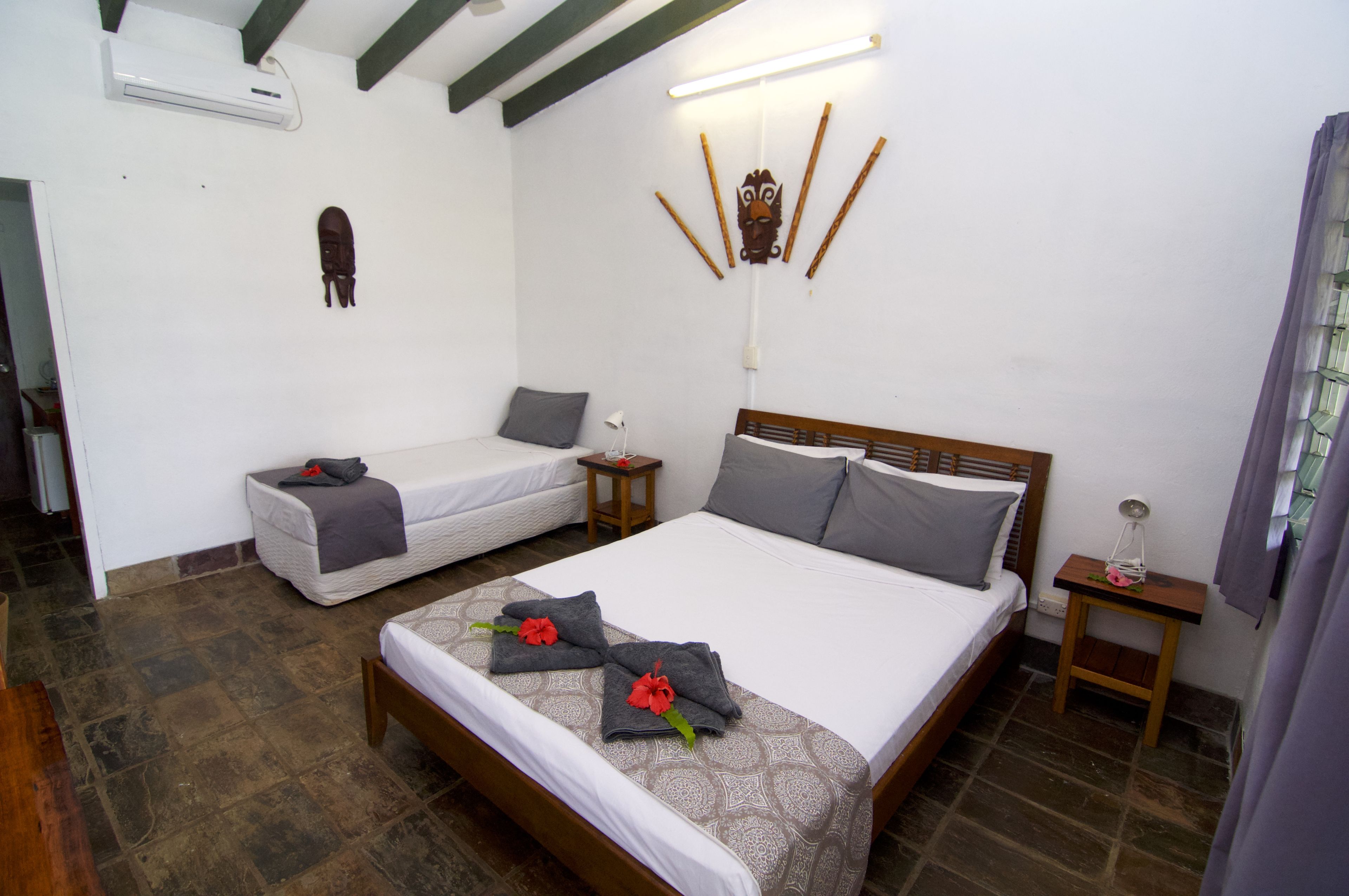 A hotel room with a large bed, a smaller bed, a wooden headboard, a nightstand, and a wall-mounted air conditioner.