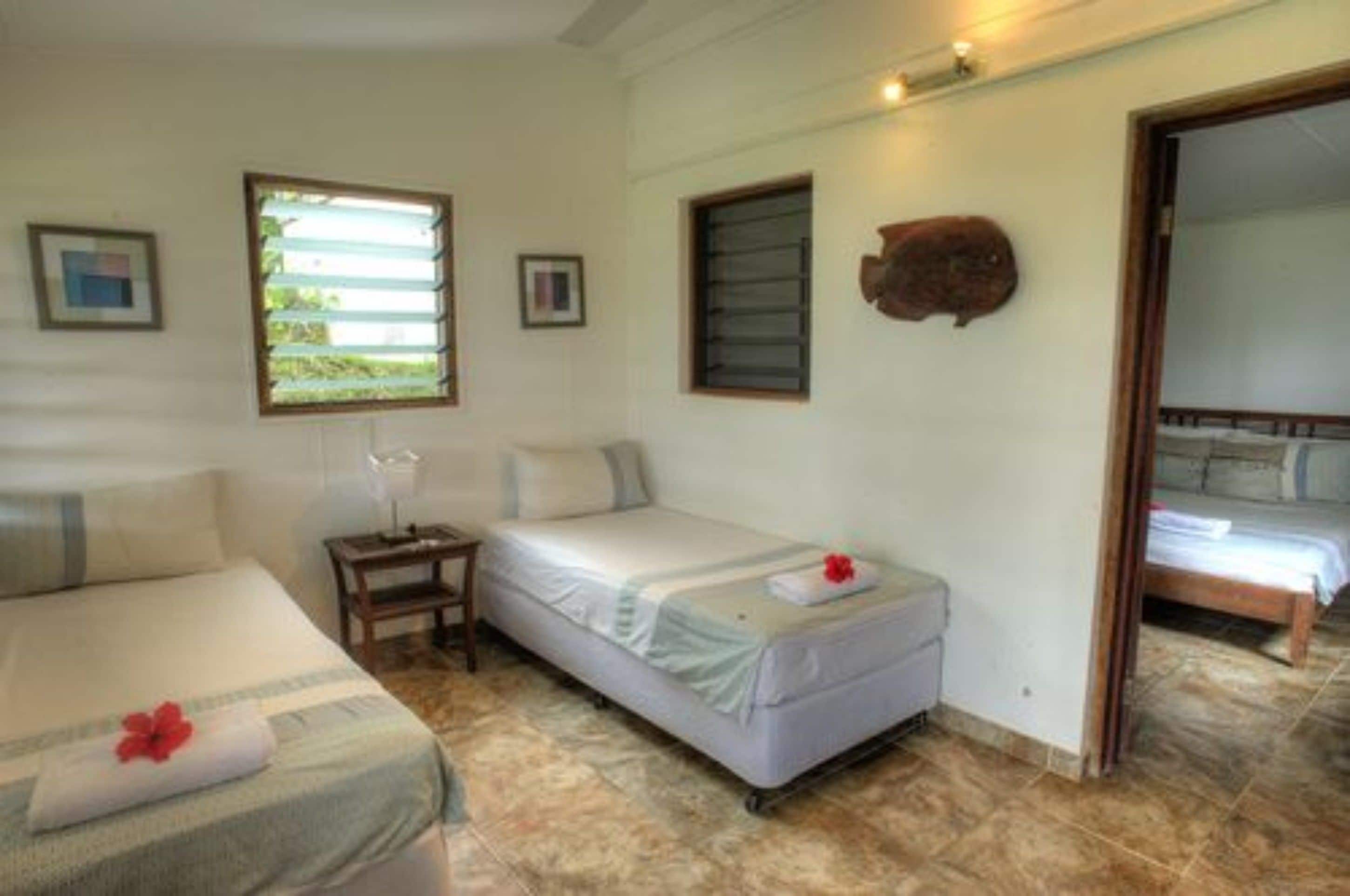 Una habitación con dos camas, una mesita y una ventana con persianas.