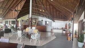 A spacious indoor area with a high ceiling and wooden beams, featuring a seating area with white wicker furniture and a central coffee table. - Deco Stop Lodge (Luganville)