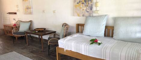 Una habitación acogedora con una cama, dos sillas de mimbre, una mesa de madera y una alfombra pequeña.