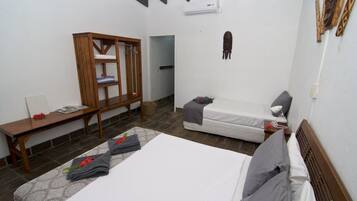 A hotel room with a large bed, a smaller bed, a wooden wardrobe, a desk, and a wall-mounted air conditioner.