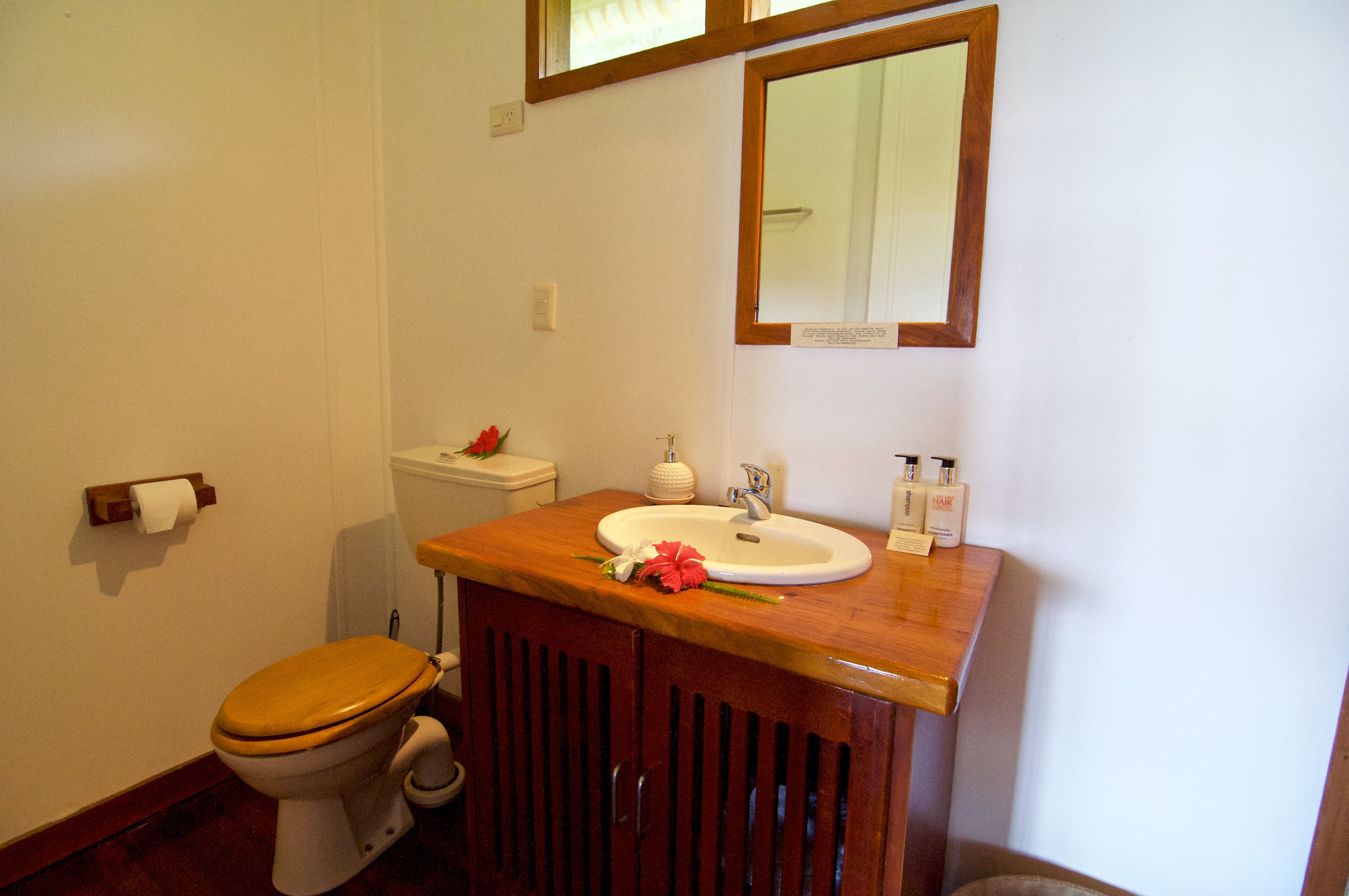 Un baño con tocador de madera, lavamanos blanco, inodoro y espejo sobre el lavamanos.