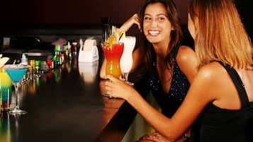 Two women sitting at a bar with various colorful drinks.