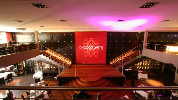 A modern interior with a central stage, multiple dining areas, and a staircase.