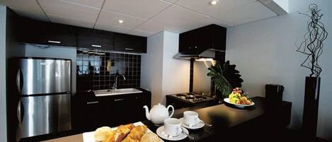 Una cocina moderna con electrodomésticos de acero inoxidable, encimera negra y un área de comedor con cruasanes y fruta.