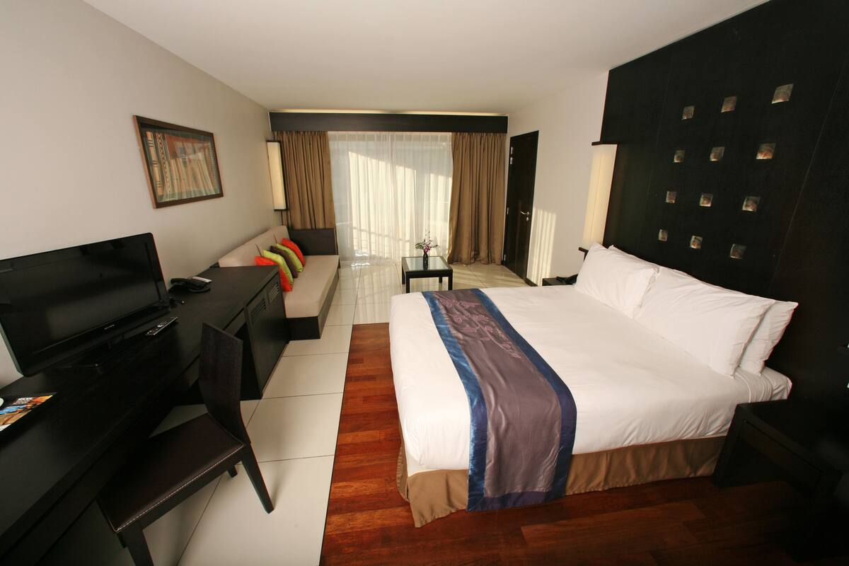 Een hotelkamer met een groot bed, een bureau met televisie, een stoel en een bank met kleurrijke kussens.
