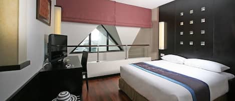 Habitación de hotel con cama, escritorio con computadora, silla, ventana con vista y cortina roja.