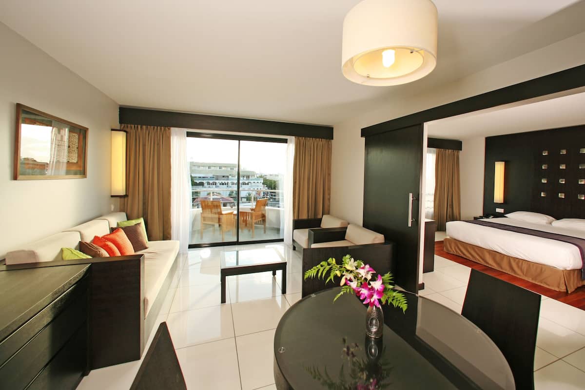 Een moderne hotelkamer met een bed, een bank, een eettafel en een balkon met uitzicht op gebouwen.