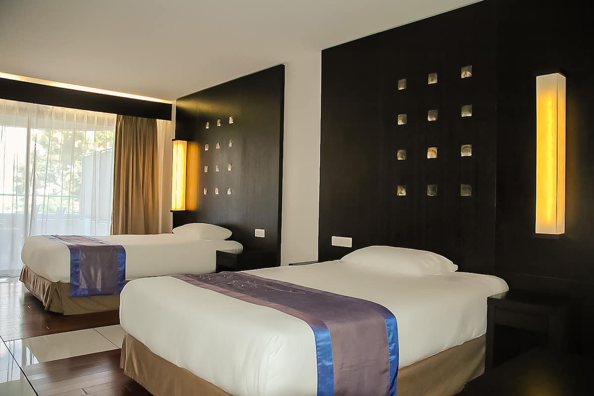 Een hotelkamer met twee bedden, een groot raam met gordijnen en wandlampen.