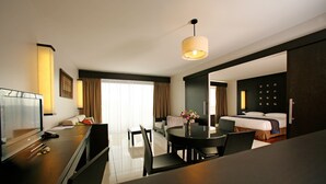 A hotel room with a dining area, a bed, a TV, and a large window with curtains.
