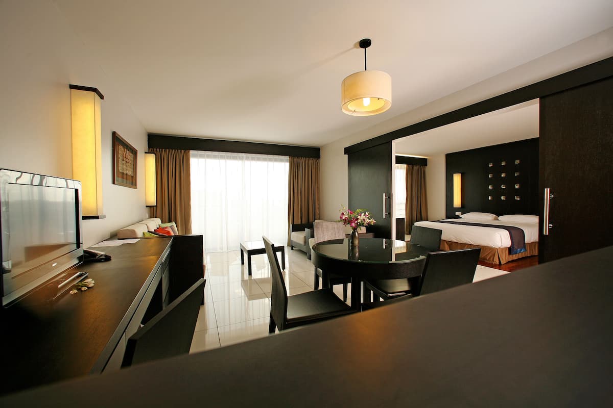 Een hotelkamer met een zithoek, een bed, een televisie en een groot raam met gordijnen.