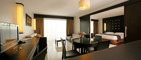 A hotel room with a dining area, a bed, a TV, and a large window with curtains.