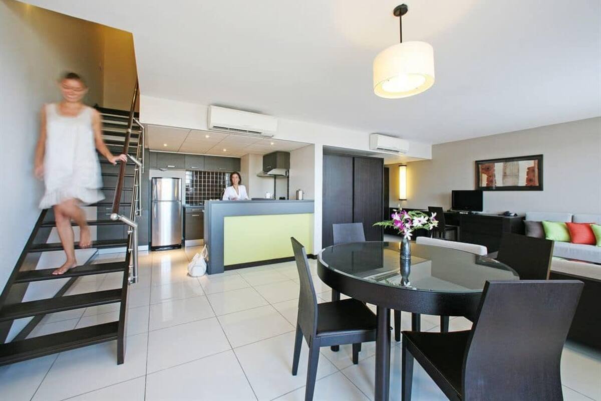 Een moderne hotelkamer met een trap, een eethoek en een keuken op de achtergrond.