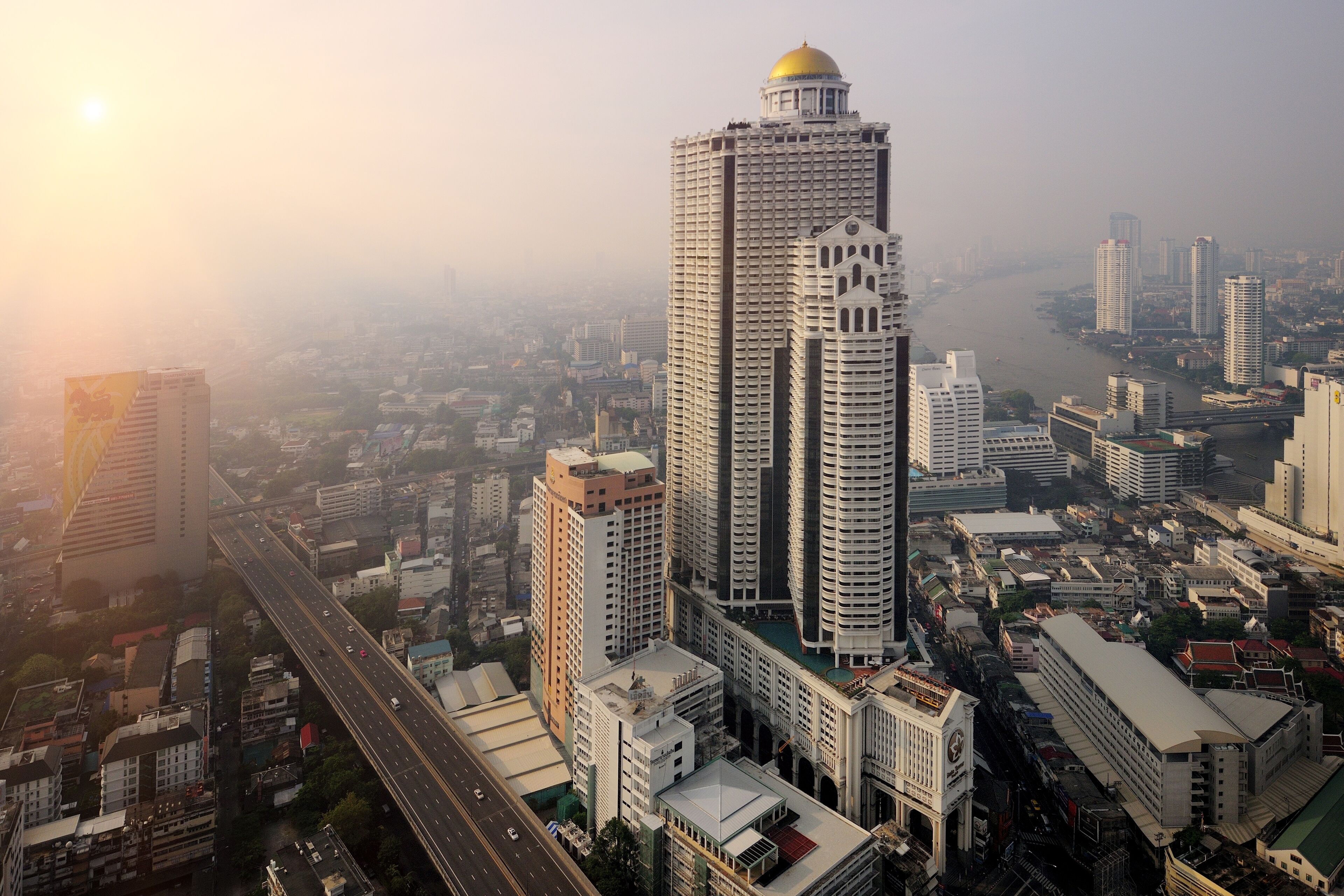 A high-rise building with a prominent dome, surrounded by other tall buildings and a busy road.