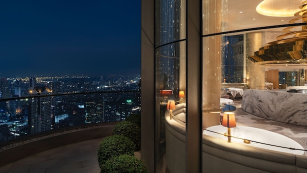 Une chambre d’hôtel située dans un immeuble de grande hauteur, offrant une vue sur la ville, dotée d’un intérieur moderne et d’un grand canapé incurvé.