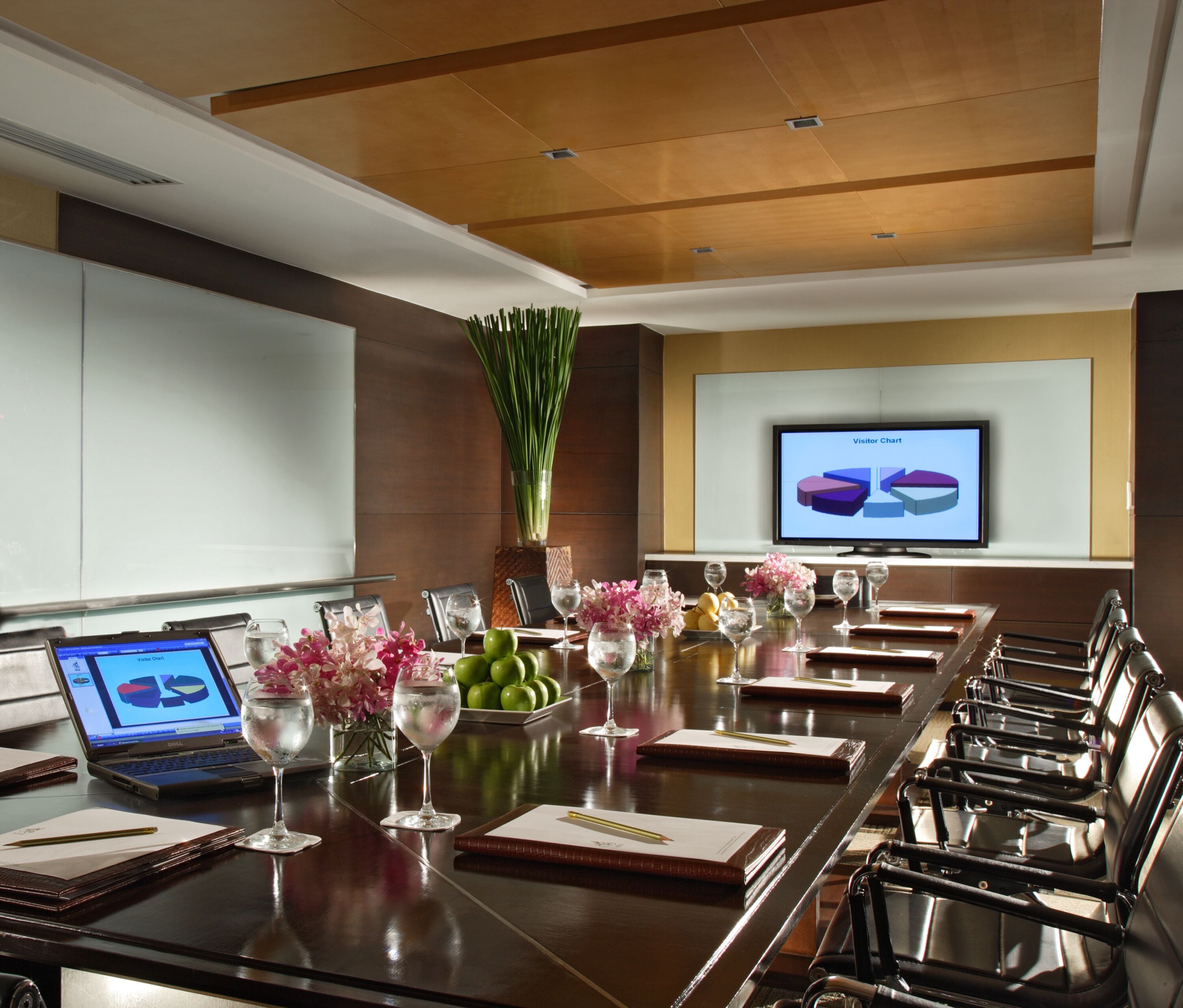 A conference room with a long table, laptops, notebooks, and a large screen displaying a pie chart.