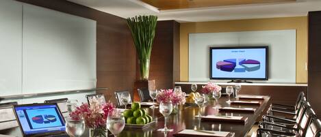 A conference room with a long table, laptops, notebooks, and a large screen displaying a pie chart.