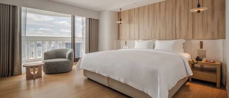 A modern hotel room with a large bed, a round chair, a nightstand with a phone, and a view of the city.